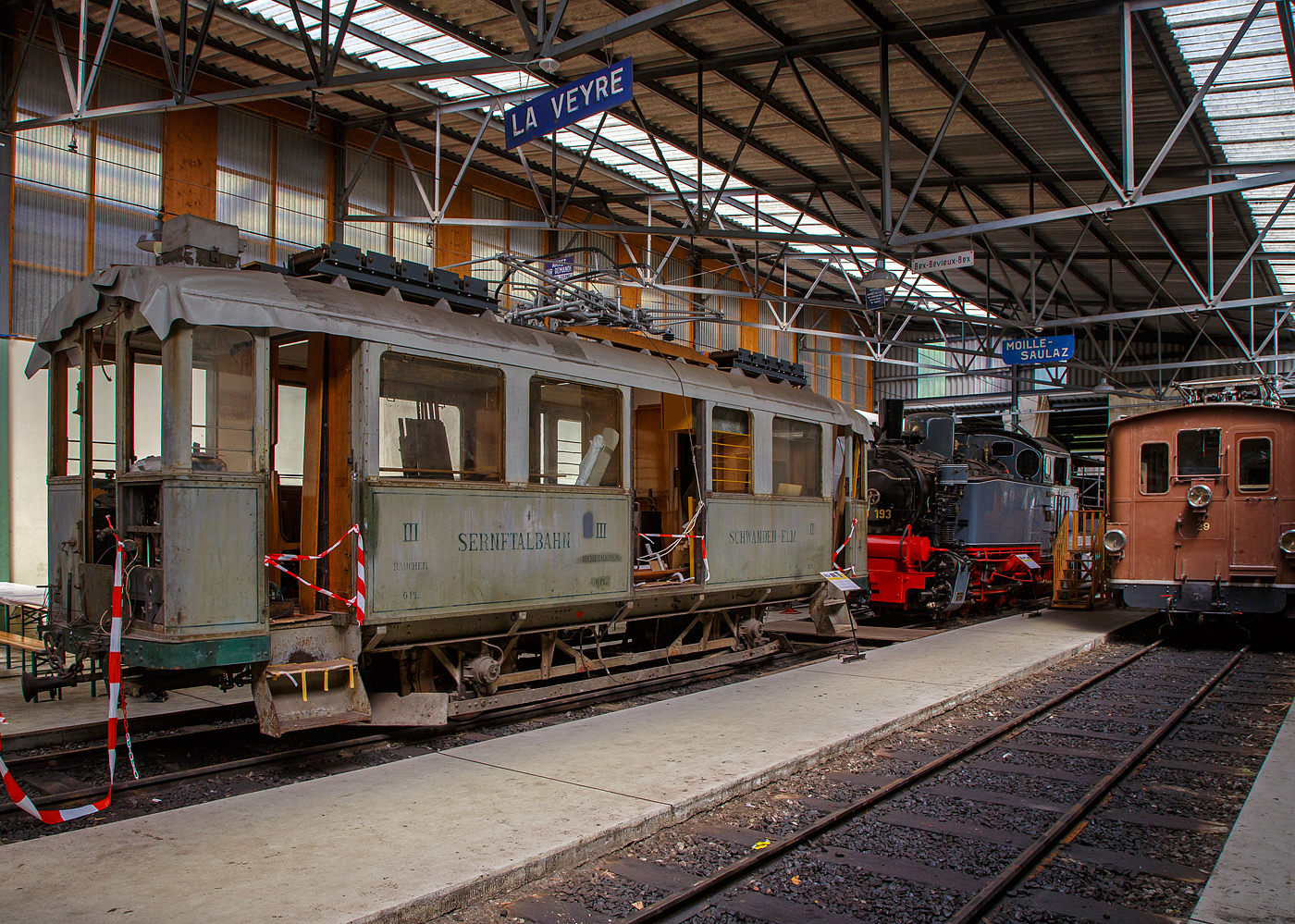 Noch in der Restaurierung (Aufarbeitungsfase) der 2./3. Klasse elektrische Personentriebwagen mit Gep�ckabteil der ehemalige Sernftalbahn SeTB  BCFe 2/2 4 der Museumsbahn Blonay–Chamby, am 27.05.2023 in der Halle der (BC) in Chaulin.

Der Personen- und Gep�cktriebwagen wurde 1928 von der SIG (Schweizerische Industrie-Gesellschaft) in Neuhausen am Rheinfall und der elektrische Teil ist von der MFO (Maschinenfabrik Oerlikon gebaut, und an die SeTB geliefert. Die Sernftalbahn (SeTB) war eine elektrische Meterspurbahn (1.000 mm) im Schweizer Kanton Glarus, sie bestand von 1905 bis 1968) und f�hrte, meist auf der Talstra�e, von Schwanden aus durch das Sernftal 13,8 Kilometer entlang des namensgebenden Flusses aufw�rts bis nach Elm. Die Triebwagen wurden mit Gleichstrom (750  V, sp�ter 800 V) aus einem eigenen Wasserkraftwerk und einer Dieselmotor-Generatoren-Gruppe angetrieben. Die Betriebsleitung befand sich in Engi in der Mitte der Strecke. Nach der Einstellung der Bahn wurde der Triebwagen, wie auch der Personenwagen BC 13 und der G�terwagen K 31, 1969 an die Museumsbahn Blonay–Chamby (BC) abgegeben.

TECHNISCHE DATEN:
Spurweite: 1.000 mm
Achsfolge: A’A’
L�nge �ber Puffer : 10.420 mm
Achsstand: 4.700 mm
Triebraddurchmesser: 860 mm (neu)
Eigengewicht: 15,2 t 
Leistung: 2 � 64 kW = 128 kW (2 x 87 PS = 174 PS)
Getriebe�bersetzungen: 1:5,92
Zul. H�chstgeschwindigkeit: 30 km/h 
Stromsystem: urspr�nglich 850 V DC (Gleichstrom) / bei der BC 1.000 V
Stromabnehmer: 1 Scheren-Stromabnehmer, Bet�tigung �ber Schnur
Max. Neigung : 68 ‰  (SeTB)
Sitzpl�tze: 6 (2. Klasse), 12 (3. Klasse) 
Gep�ckabteilgr��e: 4 m�
Max. Gep�ck Zuladungsgewicht: 3,0  t

Quellen: BC