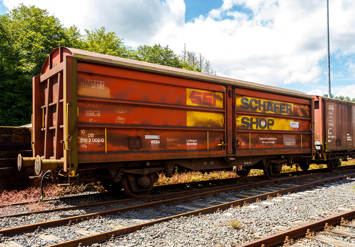Privater gedeckter Güterwagen mit Schiebewänden der Gattung Hills, 10 80 2102 002-0, WEBA 03 (10 80 DB 210 2 002-0), der Westerwaldbahn (WEBA) abgestellt am 07 Juöi 2024 auf dem Betriebshof der WEBA)auf der Bindweide bei Steinebach/Sieg abgestellt.

Der Wagen wurde 1989 von Rolanfer Matériel Ferroviaire SAS in Metz-Woippy (Frankreich) unter der Fabriknummer 534012 für die SNCB gebaut, wann er auf den Westerwald kam ist mir unbekannt.

Beschreibung:
Der Wagen hat auf jeder Längsseite vier Schiebewände, so ist es möglich jeweils eine halbe Längsseide zu öffnen. Eingesetzt wurden diese Waggons für den Transport von großen nässeempfindlichen Stückgütern (bei diesem Wagen waren es Büromöbel).

TECHNISCHE DATEN:
Spurweite: 1.435 mm
Länge über Puffer :11.690 mm
Achsabstand: 6.000 mm
Eigengewicht: 14.460 kg
Ladelänge:10.260 mm
Ladefläche: 25,8 m²
Rauminhalt: 57,41 m³
Höchstgeschwindigkeit: 100 km/h
Maximales Ladegewicht: 20,5 t (Streckenklasse C oder höher)
Bremse: WE-GP

Bei der WEBA war der Wagen auf der eigenen Strecke (Scheuerfeld – Bindweide – Weitefeld) und nur auf der DB Strecke Scheuerfeld (Sieg) – Betzdorf (Sieg) zugelassen. Die WEBA hat 2017 den Güterverkehr eingestellt. Zudem ist für den Kunden der Bahntransport von Büromöbel (von Weitefeld nach Betzdorf) nicht mehr nötig.