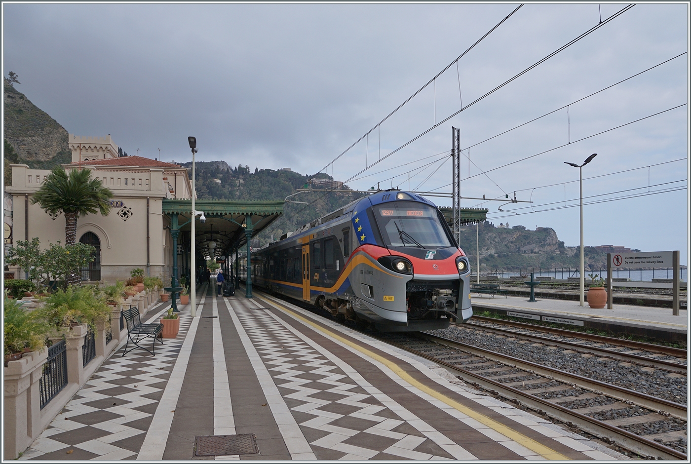 Pünktlich wie die Eisenbahn... Nachdem ein schwerer Wintersturm vom 20. bis 22. Januar 2026 besonders die Nordostküste von Sizilien verwüstet hatte, musste auf dem Abschnitt Messina - Taormina der Zugsbetrieb eingestellt werden. Die RFI musste an etlichen Küstenabschnitten die Infrastruktur wieder herrichten und dies sollte bis am 6. März dauern. Unsere Anreise nach Taormina-Giradini (bzw. Naxos) war schon lange vorher für den 7. März geplant und aus Erfahrungen bei anderen Bahnen, war ich etwas skeptisch ob der Termin für den 7. März auch eingehalten werden konnte. Doch pünktlich wie die Eisenbahn fahren seit dem 7. März wieder Züge zwischen Messina und Taormina!

Der FS Treniatila ETR 104.100 verlässt den Bahnhof von Taormina-Giardini. Der Triebzug ist als Regionalzug 12977 von Messina nach Catania Aeroporte Fontanarossa unterwegs. 

7. März 2026