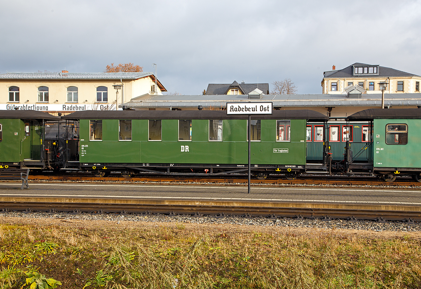 Vierachsiger 750 mm-Schmalspur 2.Klasse Altbau Personenwagen mit Traglastenabteil, offenen Plattformen und Holzdach, SDG 970-575 (ex DB 970-557, ex DR 970-557), der Gattung KB4 tr, der SDG - S�chsische Dampfeisenbahngesellschaft mbH abgestellt im Zugverband am 07.12.2022 beim Schmalspur-Bahnhof Radebeul Ost (L��nitzgrundbahn). Hier in der ehem. DR Erscheinungsbild. 

Der Wagen wurde 1926 von der von der Waggon- und Maschinenfabrik Aktien-Gesellschaft vorm. Busch in Bautzen gebaut. Er ist als Traglastenwagen (f�r Kinderwagen etc.) ausgef�hrt. Die Altbau Ausf�hrung kann man gut an den Fenstern erkennen, zum �ffnen wird hier die ganze Scheibe noch unten geschoben.

Diese in den zwanziger Jahren gefertigten Wagen, haben gegen�ber den Erstserien nun blechbeplankte Au�enw�nde. Auch hielten Dampfheizung und Saugluftbremse Einzug. Die bei der Deutschen Reichsbahn verbliebenen Wagen wurden teilweise umgebaut und technisch angepasst. Ende der siebziger Jahre wurde ein Teil der Wagen modernisiert. Diese erhielten dabei ein v�llig ge�ndertes �u�eres Erscheinungsbild. Mehrere dieser Traglastenwagen sind heute noch bei verschiedenen s�chsischen Schmalspurbahnen und Museumsbahnen im Einsatz.

Die �lteren Nummern der Deutsche Reichsbahn (1950 - 1958) 7.xxxx, der Deutsche Reichsbahn Gesellschaft / DR (1927 - 1950) K 3xx, sowie der K�niglich S�chsische Staatseisenbahnen (1913 – 1927) xxx K, sind mir leider unbekannt.

TECHNISCHE DATEN:
Spurweite: 750 mm
Anzahl der Achsen: 4
L�nge �ber Puffer: 12.800 mm
Drehzapfenabstand: 7.500 mm
Achsabstand im Drehgestell: 1.300 mm
Eigengewicht: 10 t
Sitzpl�tze: 42 (in der 2. Klasse)
Bremse: KE-P