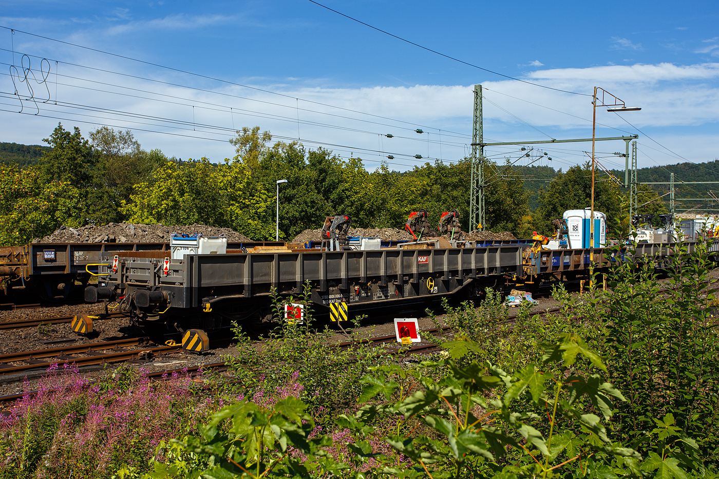 Vierachsiger Drehgestell-Flachwagen, mit festen Seitenwänden und Stirnwandklappen, 37 80 4806 006-5 D-KAF, der Gattung Slmns1, der KAF - Falkenhahn Bau AG (Kreuztal), beladen mit Material und Equipment für die Baustelle, abgestellt am 26 August 2025 im Zugverband in Scheuerfeld/Sieg nahe der Baustelle. 

TECHNISCHE DATEN:
Spurweite: 1.435 mm (Normalspur)
Gattung/Bauart: Slmns1
Anzahl der Achsen: 4 in 2 Drehgestellen
Länge über Puffer: 16.740 mm
Drehzapfenabstand:  11.700 mm
Achsabstand in den Drehgestellen: 1.800 mm
Eigengewicht: 23.900 kg
Ladelänge: 15.500 mm
Ladefläche: 43,3 m²
Maximale Ladegewicht: 66,1 t (Streckenklasse D)
Höchstgeschwindigkeit: 100 km/h (beladen) / 120 km/h (leer)
Kleinster befahrbarer Gleisbogenhalbmesser: R 45 m
Feststellbremse: ja
Bauart der Bremse: KE-GP-A (K), Max. 58 t
Bremssohle: C 810
Intern. Verwendungsfähigkeit: TEN-GE / G1

Bedeutung der Gattungsbezeichnung (Slmns):
S = Flachwagen mit Drehgestellen in Sonderbauart
l = ohne Rungen
m = mit vier Radsätzen, Ladelänge 15 m bis unter 18 m
n = mit vier Radsätzen höchste Lastgrenze über 60
s = lauffähig (beladen) bis 100 km/h

Quelle: laut Anschriften