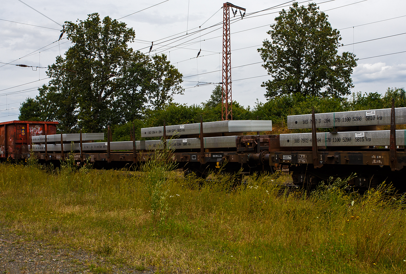 Vierachsiger Drehgestellflachwagen mit Rungen und Stirnwandklappen, jedoch ohne Seitenwandklappen (Rungenwagen), 31 80 3914 896-6  D-DB, der Gattung Rs 689, der DB Cargo AG, am 19 Juli 2024 im Zugverband bei einer Zugdurchfahrt durch Rudersdorf (Kreis Siegen). Beladen ist der Wagen hier mit 9 Aluminium-Brammen mit einem Stückgewischt von 5.600 bis 6.600 kg. So ist der Wagen gemäß Lastgrenzenraster für die Streckenklasse C gut ausgeladen (aber nicht überladen). 

Der Wagen wurde 1977 von MAN in Nürnberg gebaut.