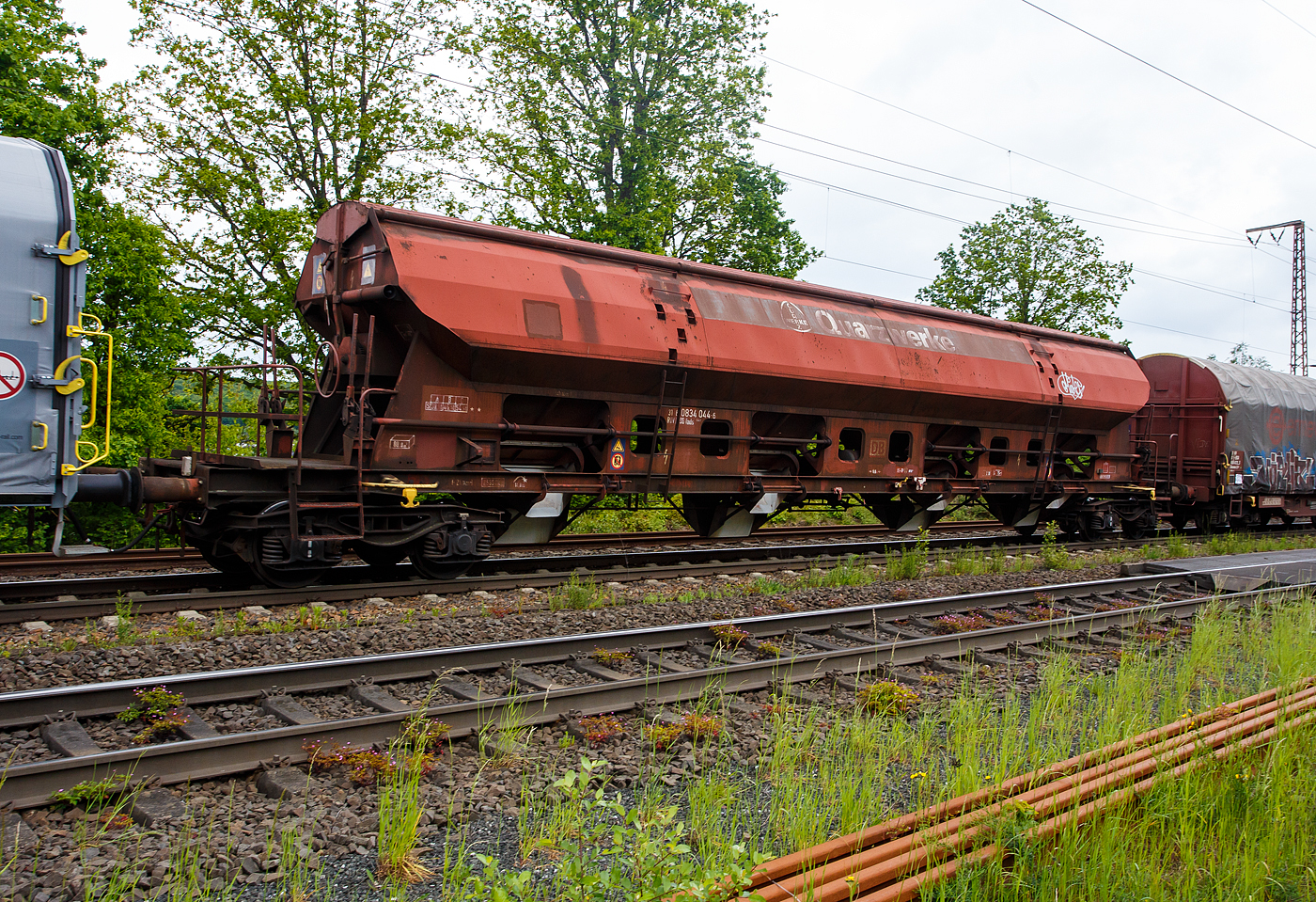 Vierachsiger gedeckter Drehgestell-Schüttgutwagen mit dosierbarer Schwerkraftentladung, 31 80 083 4 044-6 D-DB, der Gattung Tads 960, der DB Cargo AG am 22 Mai 2023 im Zugverband bei einer Zugdurchfahrt in Wilnsdorf-Rudersdorf.

Die Wagen sind geeignet für den Transport von witterungsempfindlichen Schüttgütern. Die Ladegüter sind z.B. Quarzsand, Dolomit, Anthrazit, Gipsstein, Kalk, Holzpellets, Petrolkoks, Kaolin und Paraffine. Die Beladung erfolgt über ein einteiliges Schwenkdach. Sie besitzen eine gleisseitige dosierbare Entladeeinrichtung. Ein Teil der Wagen ist für den Transport von Quarzsand mit speziellen Dichtungen an den Auslaufrutschen ausgestattet.

Die Wagen der Bauart Tads 960 sind durch Umzeichnung aus der Bauart Tads 959 hervorgegangen. Der Wagen dient wegen seiner besonderen Schieberabdichtung dem Transport von feinkörnigen, nässeempfindlichen Schüttgütern, besonders für Quarzsand. Der Transport grobkörniger oder kantiger, schwerer Güter (z. B. Kies, Schlacke, Schotter) ist wegen einer möglichen Beschädigung der Innenbeschichtung nicht zulässig. Der Wagen kann wahlweise nach der einen oder anderen Seite oder gleichzeitig nach beiden Seiten entladen werden. Die regelbare Entladung ermöglicht die Beschickung von Förderbändern. Die schwenkbaren Auslaufrutschen gestatten den Einsatz des Wagens für die Entladung in Bunkern oder auf seitliche Förderbänder.

Das Untergestell ist aus Walzprofilen (St 52-3) geschweißt. Der Wagenkasten ist ebenfalls geschweißt. Für die 3 mm dicken Kastenbleche wurde St 52-3 mit Cu-Zusatz verwendet. In jeder Seitenwand sind vier exzentrisch gelagerte Rundschieber angeordnet. Jeder Schieber kann einzeln mit einem Handhebel von der Bühne aus geöffnet und geschlossen werden. Die Unterkanten der festen Auslaufrutschen liegen bei leerem Wagen 720 mm über SO. Die Unterkanten der beweglichen Auslaufrutschen liegen bei leerem Wagen im ausgeschwenkten Zustand 385 mm über SO.

Zum Beladen des Wagens wird das Schwenkdach von der Bedienungsplattform aus mit einem Handrad geöffnet. Dabei wird eine über die ganze Wagenlänge reichende Öffnung von 1 200 mm Breite freigegeben. Das geöffnete Dach bleibt innerhalb der Wagenbegrenzungslinie, so dass Verschiebebewegungen auch bei geöffnetem Schwenkdach möglich sind.

Das Entfernen von Ladegutresten in der Be- oder Entladestraße ist nur durch leichte Gummihammerschläge auf die äußeren Behälterwandungen gestattet oder durch den Einsatz von Pressluftlanzen im Laderaum.

TECHNISCHE DATEN:
Hersteller: Waggonfabrik Talbot in Aachen
Baujahr: ab 1973 (Umzeichnung 2003 – 2006)
Spurweite: 1.435 mm
Länge über Puffer: 21.640 mm
Drehzapfenabstand: 16.600 mm
Achsabstand im Drehgestell: 1.800 mm
Beladeöffnung: 16.800 x 1.200 mm
Eigengewicht: 25.350 kg
Höchstgeschwindigkeit: 100 km/h (beladen) / 120 km/h (leer)
Maximales Ladegewicht: 54,5 t (Streckenklasse C oder höher)
Kleinster bef. Gleisbogenradius: 75 m
Rauminhalt: 80,0 m³
Bremse: KE-GP-A (LL)
Intern. Verwendungsfähigkeit: RIV

Die Bedeutung der Gattungs- und Kennbuchstaben (hier Tads):
T - Wagen mit öffnungsfähigem Dach 
a - mit vier Radsätzen
d - mit Schwerkraftentladung, dosierbar, wahlweise zweiseitig, hochliegend
s - Höchstgeschwindigkeit 100 km/h (beladen)