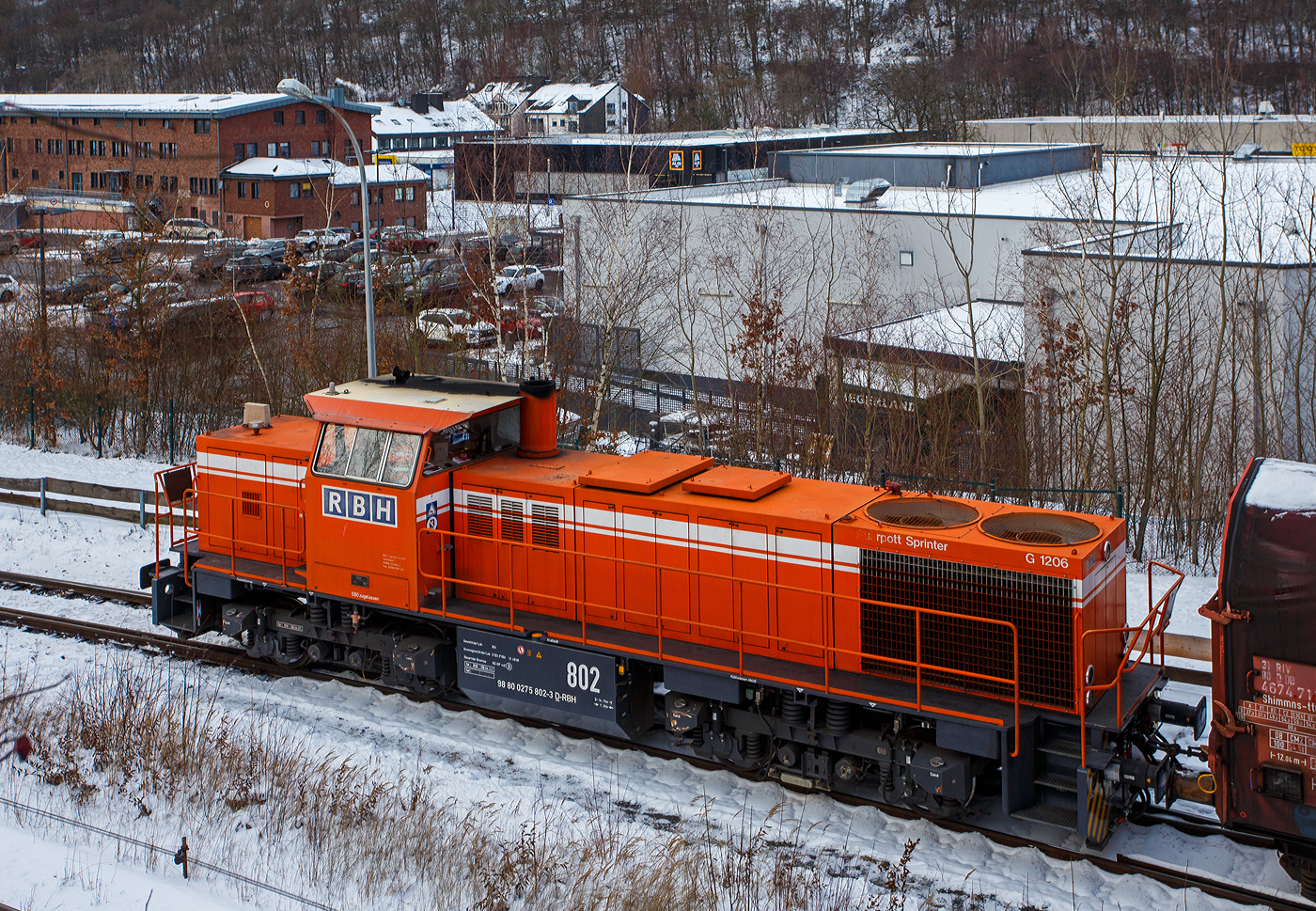 Zurzeit ist die RBH 802 „Ruhrpott Sprinter“ / 275 802-3 (98 80 0275 802-3 D-RBH), eine MaK G 1206 der RBH - RAG Bahn und Hafen GmbH (Gladbeck), an die KSW (Kreisbahn Siegen-Wittgenstein) vermietet. Hier steht sie mit einem Übergabegüterzug, auf dem Rbf der KSW in Herdorf (Betriebsstätte Freien Grunder Eisenbahn- NE 447) vor der Gleisspeere zur Hellertalbahn, zur Abfahrt bereit. Der Zug geht dann via Betzdorf/Sieg und Siegen zum Gbf der DB Cargo in Kreuztal.

Die MaK G 1206 wurde 1997 von der Siemens Schienenfahrzeugtechnik (SFT) in Kiel-Friedrichsort unter der Fabriknummer 1000901 gebaut und an die damalige RAG - Ruhrkohle AG, RAG Bahn- und Hafenbetriebe in Gladbeck als RAG 802 ausgeliefert. Sie war erst die zweite gebaute Lok der erfolgreichen Typs G 1206 aus dem 3. Typenprogramm. Im Jahr 2004 erfolgte die Umfirmierung der RAG in RAG Bahn und Hafen GmbH (RBH) und nach der Übernahme durch die DB Schenker Rail Deutschland AG (heute DB Cargo) erfolgte 2006 die Umfirmierung in RBH Logistics GmbH. 

Die SFT war die Nachfolgefirma der Krupp Verkehrstechnik GmbH bzw. der früheren Maschinenbau Kiel GmbH (MaK). Die SFT wurde am 1. Oktober 1998 von Siemens an die Vossloh AG verkauft, in Vossloh Schienenfahrzeugtechnik (VSFT) umbenannt und firmierte seit 23. April 2004 als Vossloh Locomotives GmbH. Die Vossloh-Lokomotiven aus Kiel trugen das Kürzel MaK in der Fahrzeug-Typenbezeichnung. Nach der Fokussierung von Vossloh auf den Bereich Schiene erfolgte 2019 ein weiterer Verkauf an die Chinesische CRRC Zhuzhou Locomotive Co., Ltd.

Die Lok (MaK G 1206):
Die MaK G 1206 ist im schweren Rangier- und Streckendienst einsetzbar. Sie wurde 1997 zum ersten Mal gebaut, erster Kunde war die RAG, somit diese (die 804) erst die Vierte der Serie. Bis 2016 wurden insgesamt 323 Fahrzeuge der Baureihe G 1206, in 5 verschiedenen Varianten, produziert. Sie wurden nach Deutschland, Österreich, der Schweiz, Luxemburg, Italien, Spanien, den Niederlanden und nach Frankreich verkauft worden. Allein 23 Lokomotiven fahren als BB 61000 bei der SNCF, davon sechs mit MTU-Motor (Die G 1206 gibt es wahlweise mit Caterpillar- oder MTU-Motor). 

Diese Lok der ersten Serie (von 11 Stück) hat einen wassergekühlten 90°V16- Zylinder-Viertakt-Dieselmotor mit Abgasturbolader und Ladeluftkühlung, sowie mit Direkteinspritzung, vom Typ MTU 16V 396 TC 14 des Herstellers MTU Friedrichshafen GmbH (MTU steht für Motoren- und Turbinen-Union). Der Motor hat ein Zylinderbohrung von 165 mm und einen Kolbenhub von185 mm, damit hat der Motor einen Hubraum von 63.3 Litern. Die Motorleistung beträgt 1.570 kW (2.135 PS) bei 1.800 U/min, solche Leitungen erbringe heute 12 Zylindermotoren. Das Strömungsgetriebe ist ein Voith L 5r4 zU2. Die Höchstgeschwindigkeit der Lok beträgt 80 km/h.

Die G 1206 nimmt im 3. Typenprogramm eine besondere Rolle ein. Sie ist nicht nur die größte und leistungsstärkste Mittelführerhaus-Lok als Schlusspunkt dieser Typenreihe, sondern hat mit ihrer Verbreitung in vielen Ländern Europas inzwischen eine gebaute Stückzahl erreicht wie noch keine unabhängig von Staatsbahnaufträgen entwickelte Standardlok aus Kiel vor ihr. Was 1997 als neue Lokgeneration für die Ruhrkohle AG begann, ist heute eine Lokomotive, die in acht europäischen Ländern bei zahlreichen Bahnen, darunter zwei Staatsbahnen, im Einsatz steht.

Mitte der 1990er Jahre entstand bei den Bahn- und Hafenbetrieben der Ruhrkohle AG Bedarf nach neuen Diesellokomotiven. Diese Maschinen sollten nicht nur im schweren internen Rangier- und Zustelldienst eingesetzt werden, sondern auch - die Möglichkeiten der Liberalisierung nutzend - mit schweren Kohlezügen auf Strecken der DB AG verkehren. Dafür benötigten die Lokomotiven eine entsprechend hohe Motorleistung und eine Höchstgeschwindigkeit, die einen freizügigen Einsatz auf DB-Gleisen zulässt.

Den Auftrag zur Entwicklung und Lieferung von elf dieser Lokomotiven bekam die damalige Siemens Schienenfahrzeugtechnik GmbH. Das Ergebnis war die G 1206, deren erstes Exemplar Ende Juli 1997 an die RAG ausgeliefert wurde. Sie ist aus der G 1205 entwickelt worden und unterscheidet sich von dieser hauptsächlich durch den Dieselmotor mit 16 statt 12 Zylindern und eine entsprechend dimensionierte Kühlanlage mit zwei Lüfterrädern. Um die größere Maschinenanlage auf der Lokomotive unterbringen zu können, ist die G 1206 fast zwei Meter länger als ihre Vorgängerin ausgeführt worden.

Die 5 verschiedenen Varianten unterscheiden sich vor allem an den verwendeten Motoren und Getrieben, wie folgt:
•	Motor MTU 16V 396 TC14 mit 1570 kW; Getriebe L 5r4 zU2; Hg 80 km/h
•	Motor MTU 16V 396 TC14 mit 1570 kW; Getriebe L 5r4 zseU2; Hg 60 / 100 km/h
•	Motor MTU 12V 4000 R20 mit 1500 kW; Getriebe L 5r4 zU2; Hg 80 km/h
•	Motor Caterpillar 3512B DI TA mit 1500 kW; Getriebe L 5r4 zU2; Hg 100 km/h
•	Motor MTU 12V 4000 R41 mit 1500 kW; Getriebe L 5r4 zseU2; Hg 60 / 100 km/h

TECHNISCHE DATEN der G 1206 der 1. Serie (RAG):
Spurweite: 1.435 mm (Normalspur)
Antriebart:  dieselhydraulisch
Achsfolge: B'B' 
Länge über Puffer: 14.700 mm
Drehzapfenabstand: 7.200 mm
Achsabstand im Drehgestell: 2.400 mm
größte Breite: 3.080 mm
Höhe über Schienenoberkante: 4.220 mm
Raddurchmesser: 1.000 mm (neu)
Motor: MTU 16V 396 TC14 
Leistung: 1.570 kW bei1.800 U/min
Strömungsgetriebe: Voith L 5r4 zU2
Anfahrzugkraft: 291 kN
Höchstgeschwindigkeit: 80 km/h
kleinster befahrbarer Gleisbogen: 60 m
Dienstgewicht: 88 t
Kraftstoffvorrat: 3.150 l
