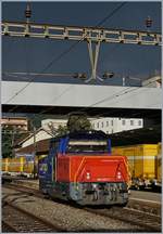 In Sierre, vor einem ziemlich dunklen Himmel zeigt sich die SBB Cargo Eem 923 027-7 im Sonnenlicht.
